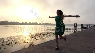 喜孕妇在夕阳下穿着绿色的衣服在河岸上奔跑